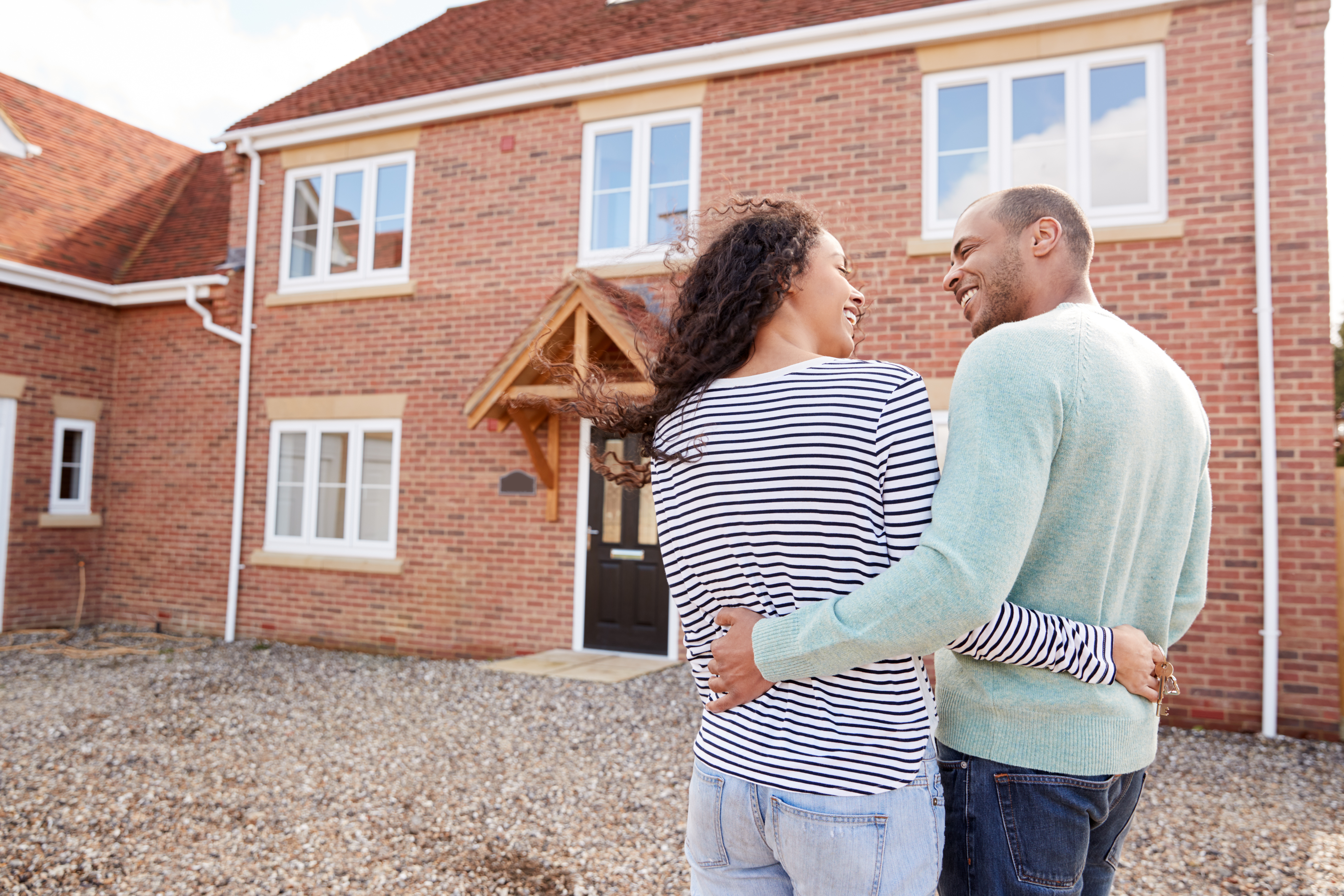 A young couple embrace in front of their new home.