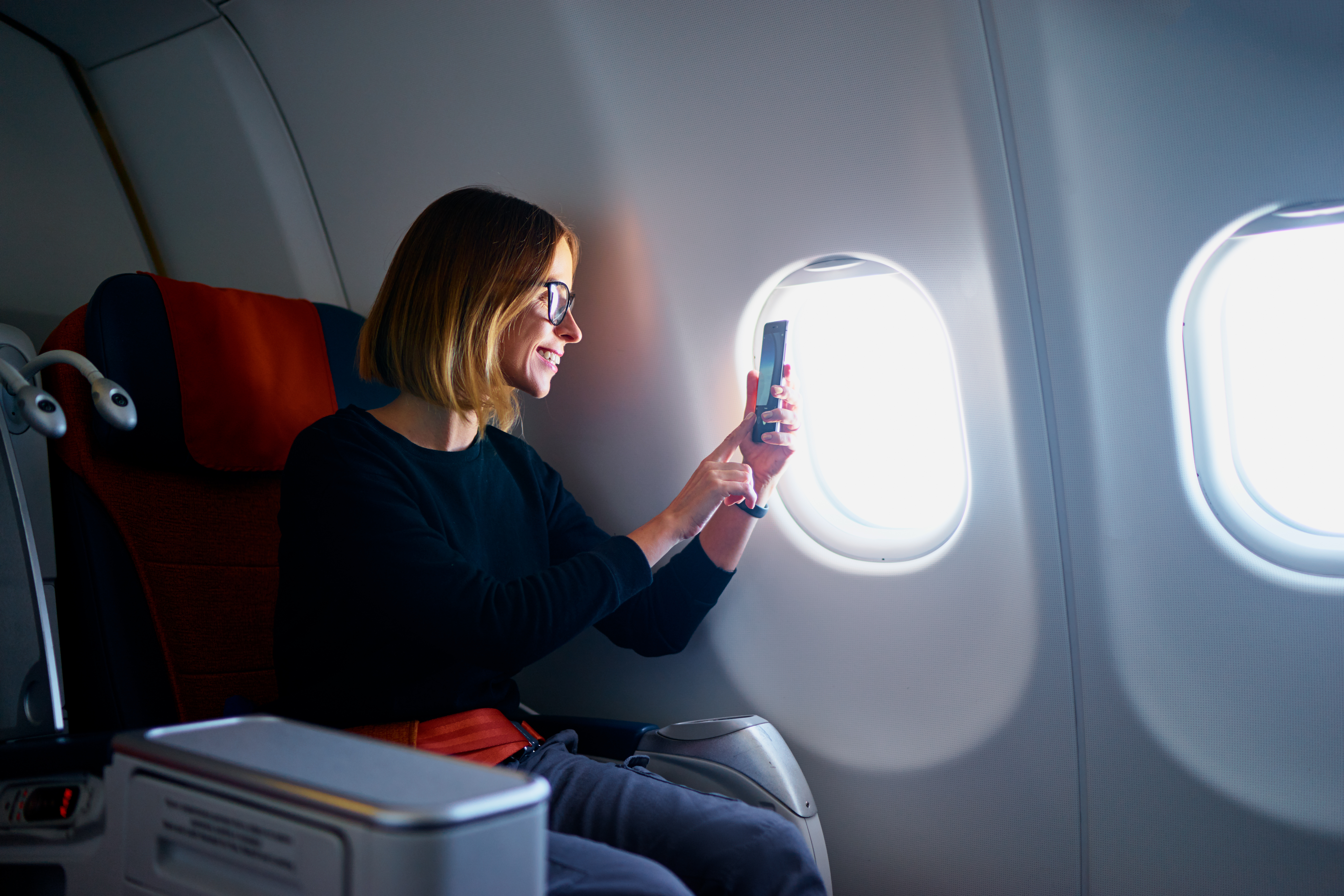 A woman uses her phone while relaxing in an airplane seat.