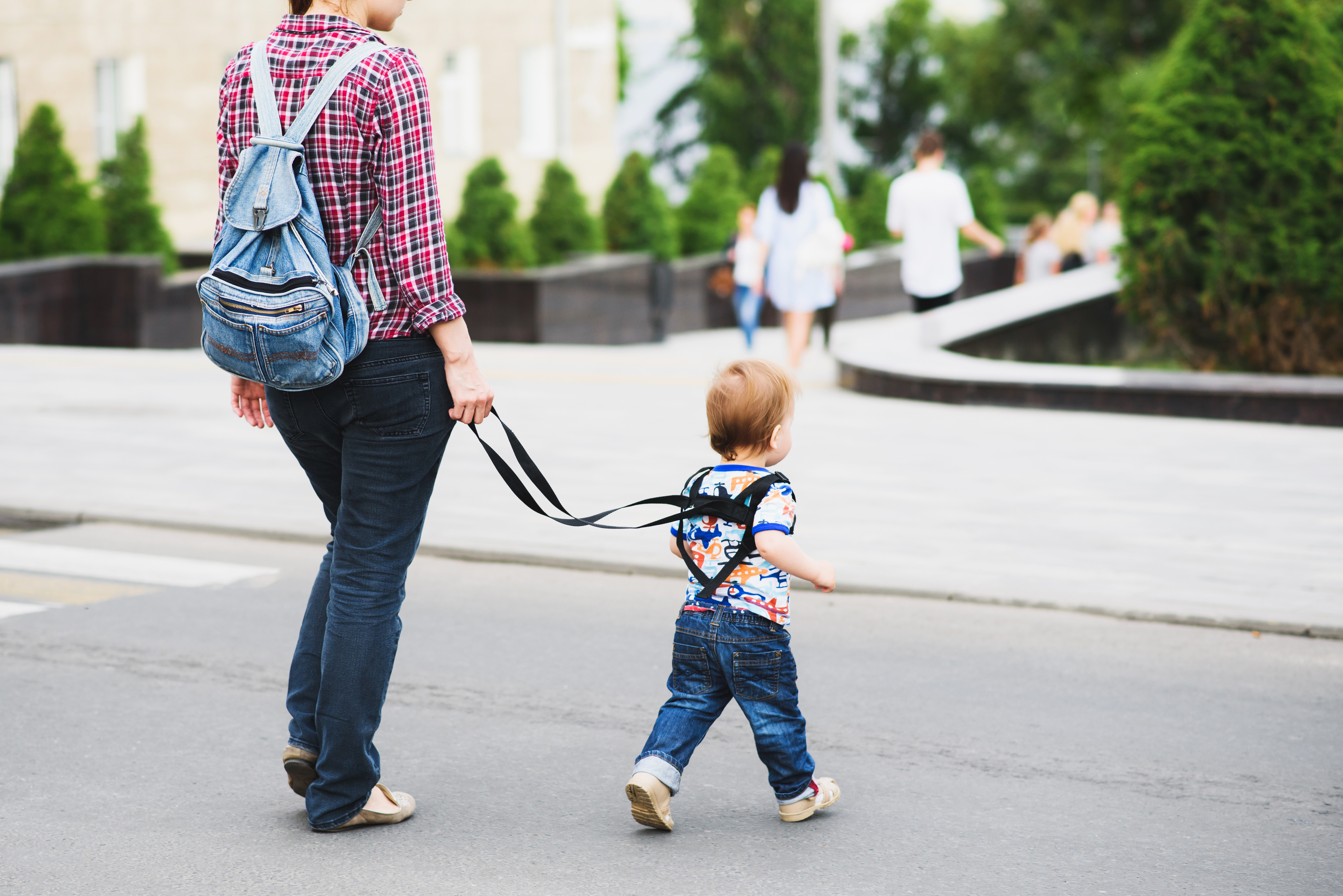 Mother holding her child's leash while walking on a street